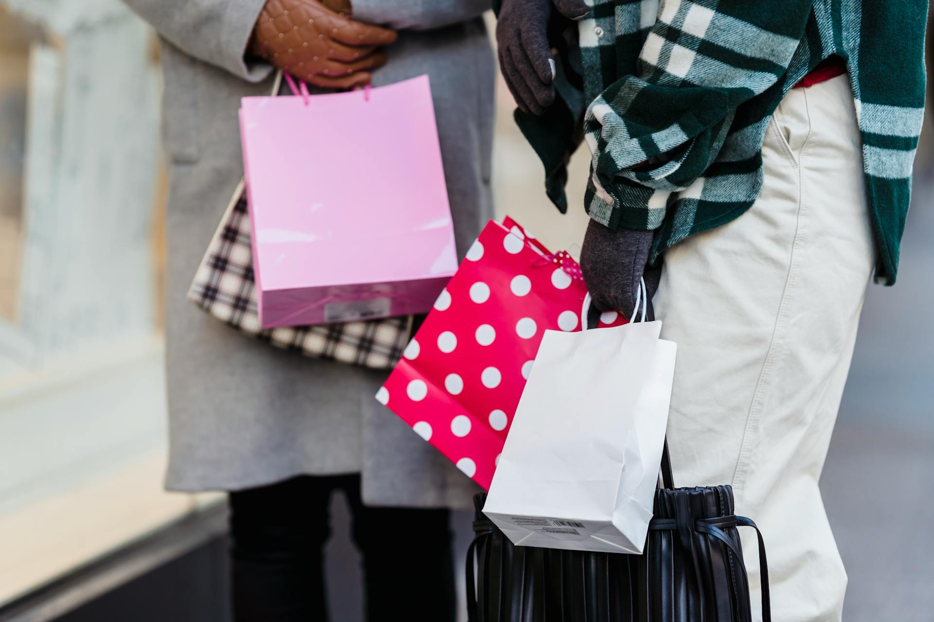 Two people holding stylish shopping bags outdoors, showcasing consumerism and fashion.