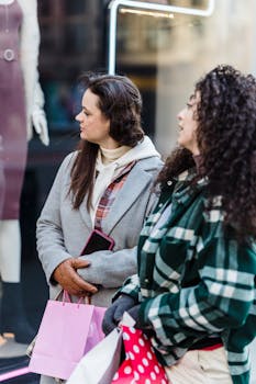 Pensive women friends in casual clothes standing with shopping bags near shop on street in daytime