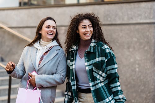 Joyful diverse ladies smiling while standing near stairs on street