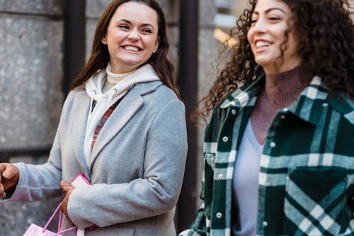 Crop joyful young multiracial female best friends in warm clothes walking on city street and laughing