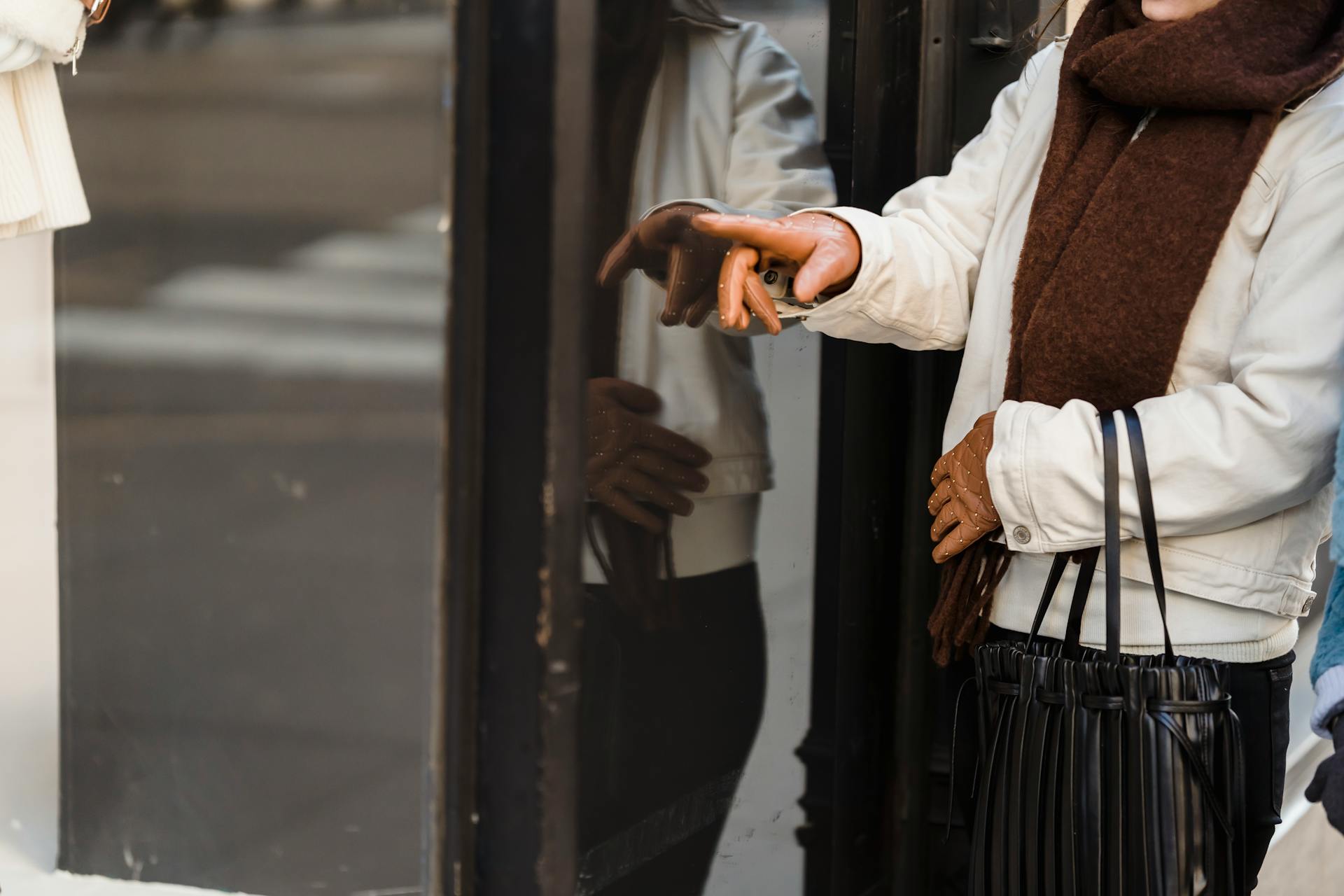 A woman wearing gloves and a scarf shopping outdoors, pointing at a store window display. Perfect for retail or fashion themes.