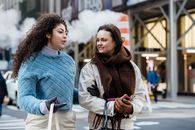 Positive stylish multiethnic women talking and crossing road in city