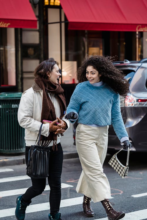 Amazed young friends in trendy clothes talking and crossing urban asphalt road of street in daytime