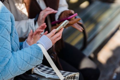 Free From above of crop anonymous friends sharing information on mobile phones in park in daytime on blurred background Stock Photo