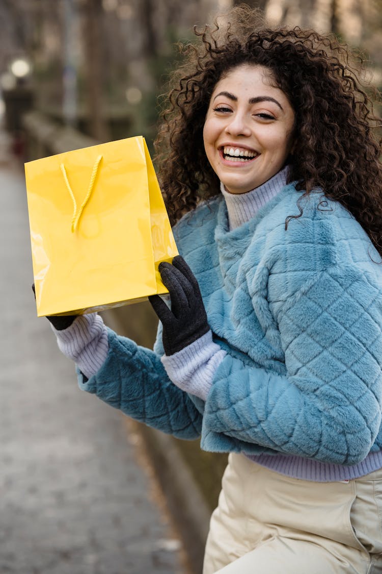 Young Smiling Woman Showing Yellow Gift Bag In Park