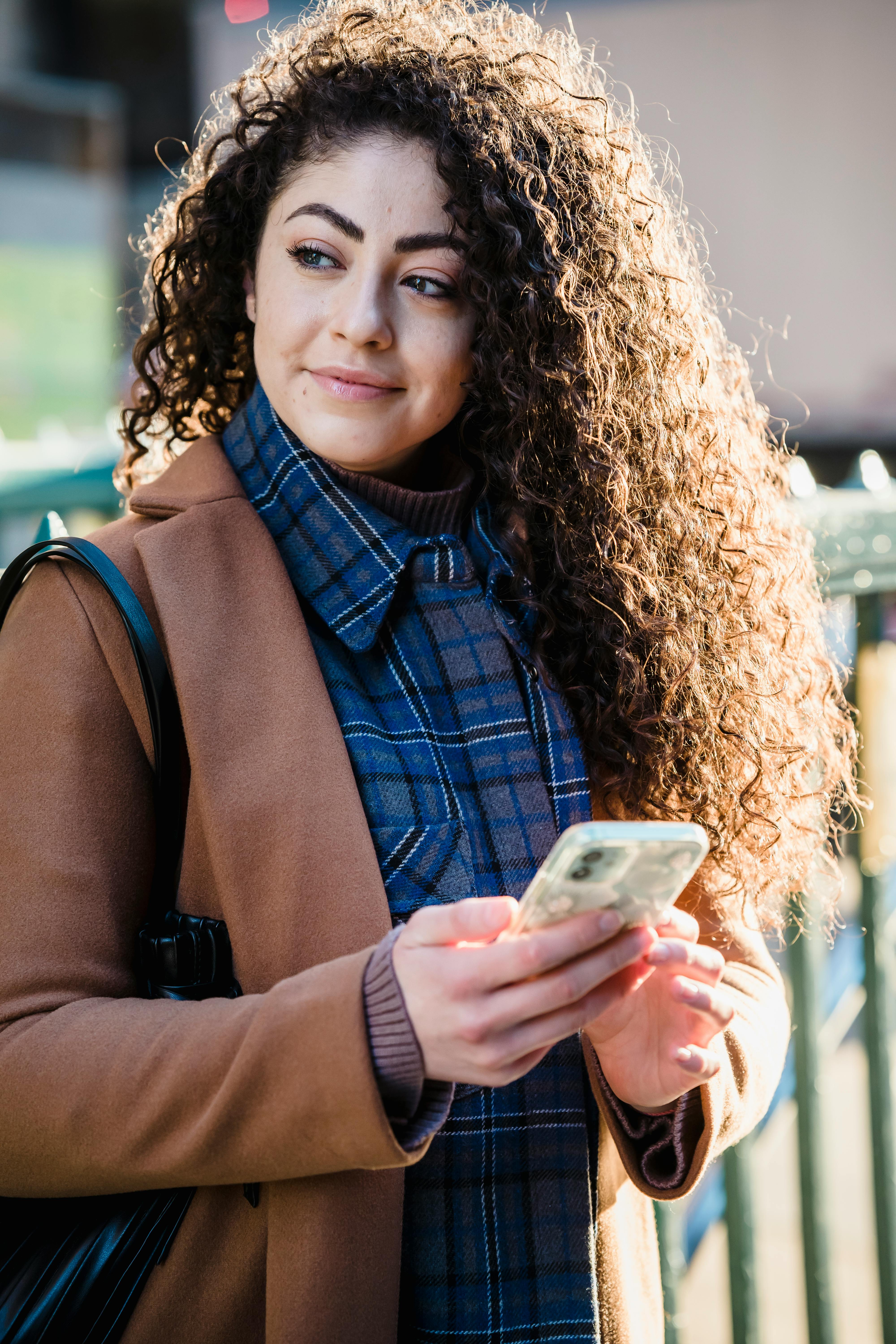 woman in trendy coat and checkered shirt using smartphone