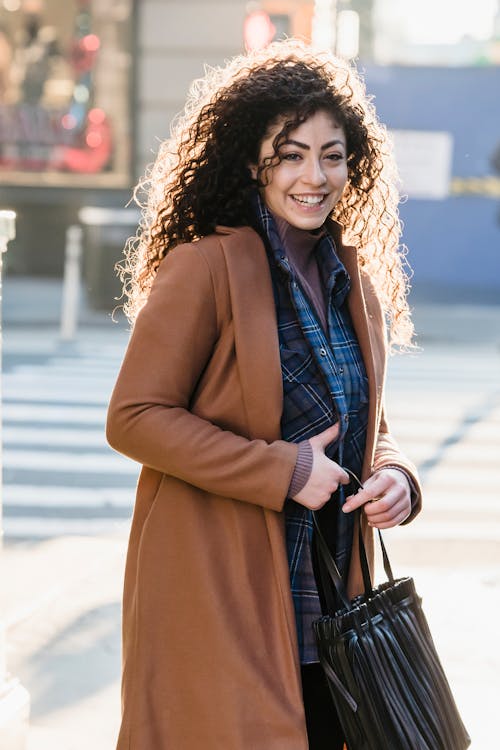 Cheerful woman with bag in trendy brown coat smiling