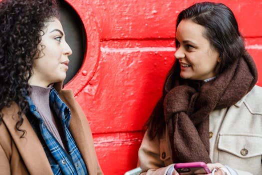 Two young women having a friendly conversation outdoors against a vibrant red backdrop.