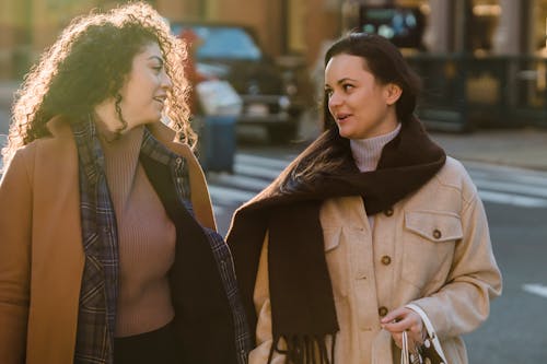 Stylish young diverse women chatting while strolling in city during weekend