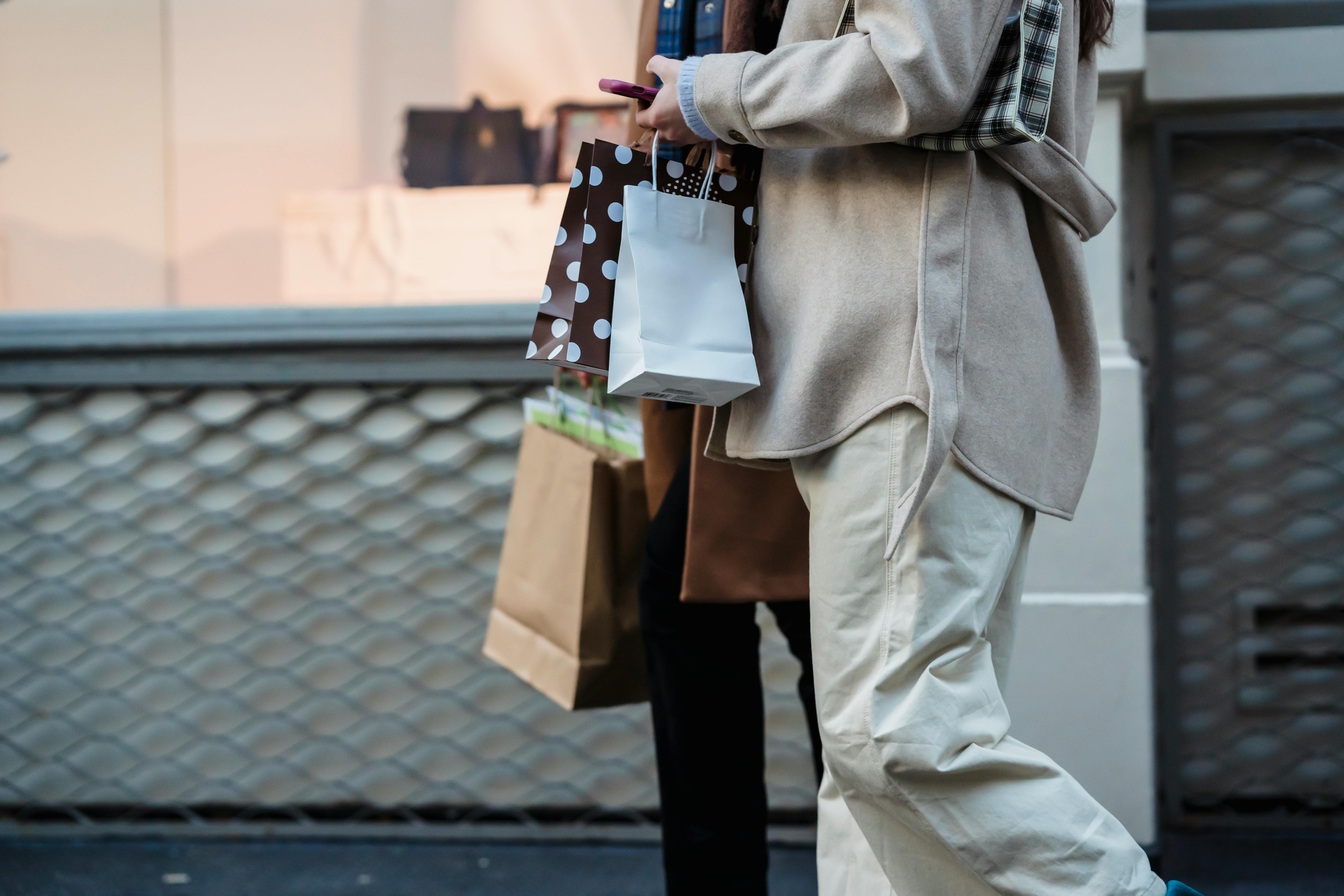crop faceless women with shopping bags and smartphone strolling on street
