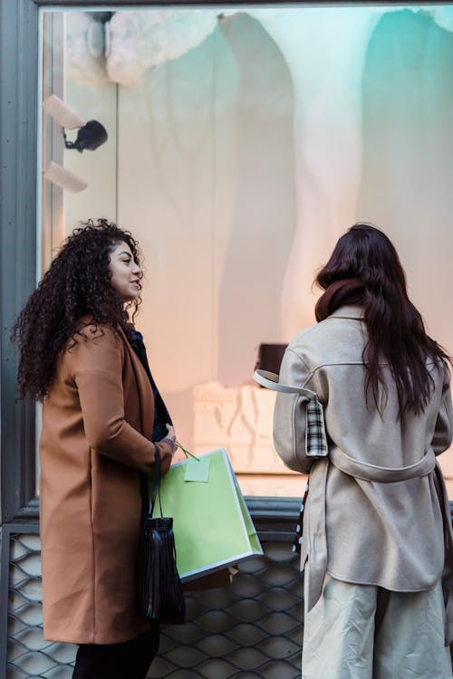 Trendy young ladies in warm stylish clothes standing near showcase of fashion store during weekend shopping in city