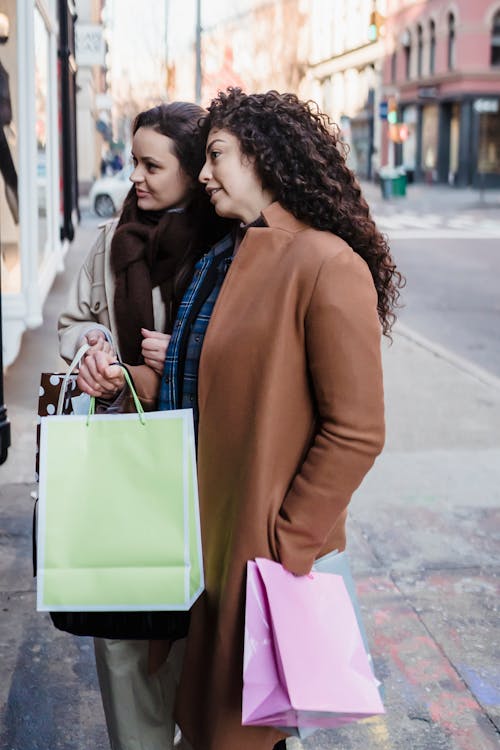 Female friend with gift bags talking on street near showcase