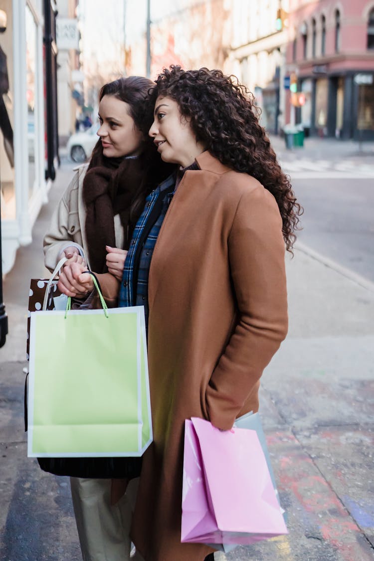 Female Friend With Gift Bags Talking On Street Near Showcase