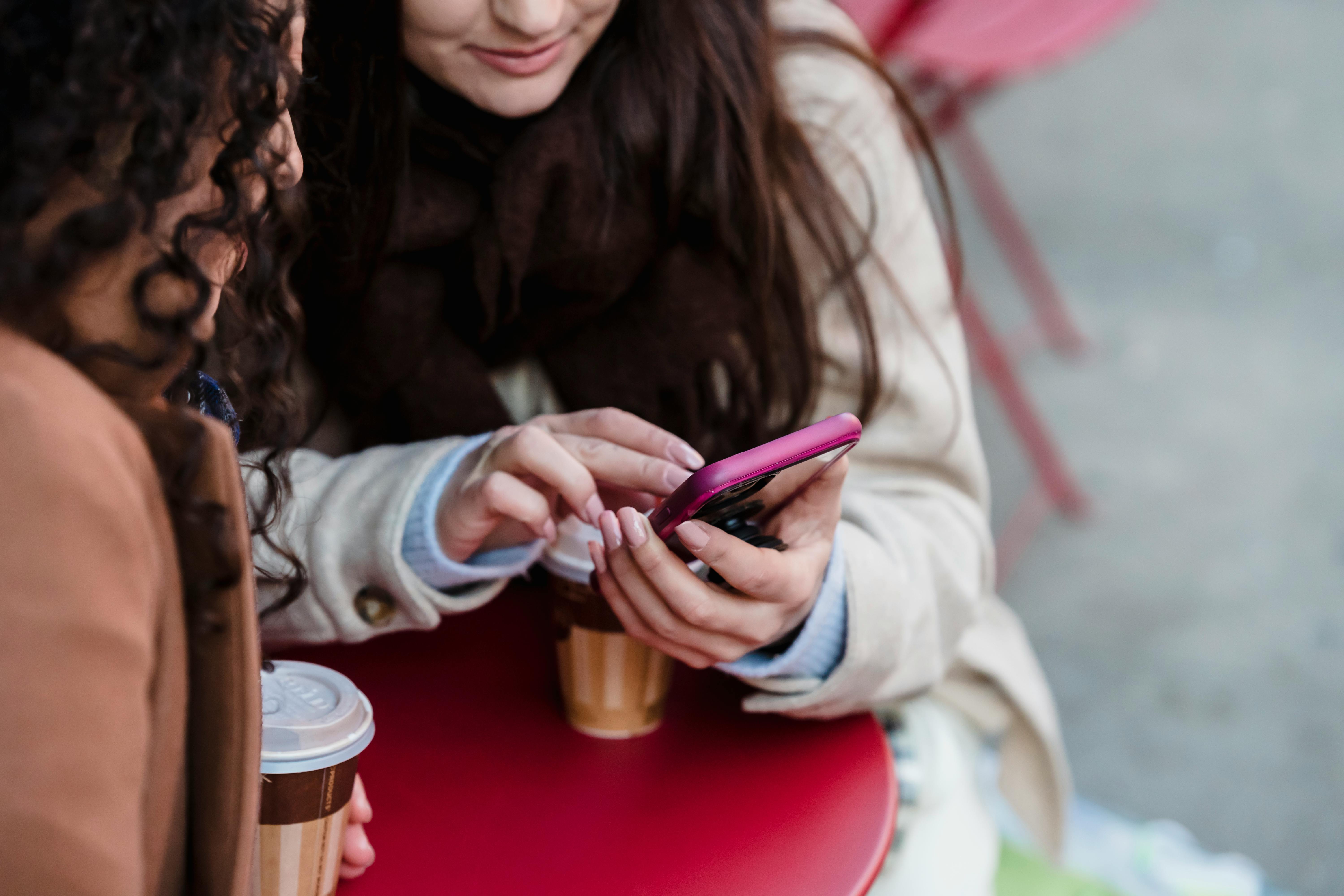 women scrolling smartphone while having coffee in cafe