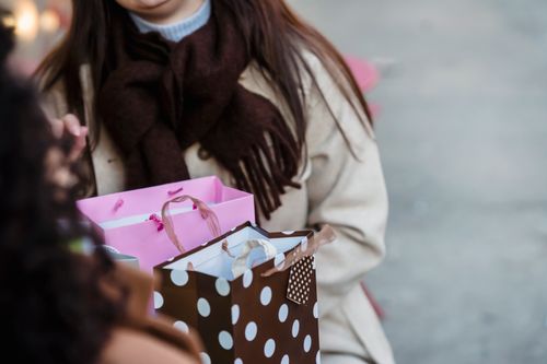 Free High angle of crop anonymous women in outerwear sitting at table with presents in paper gift bags Stock Photo