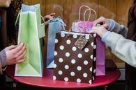 Side view of crop anonymous female friends sitting at table with various colorful gift bags bought for occasion