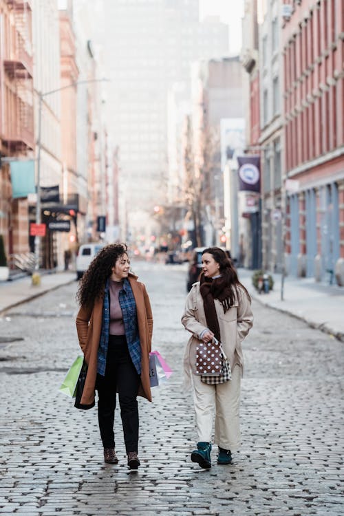 Female friends with gift bags walking on paved street