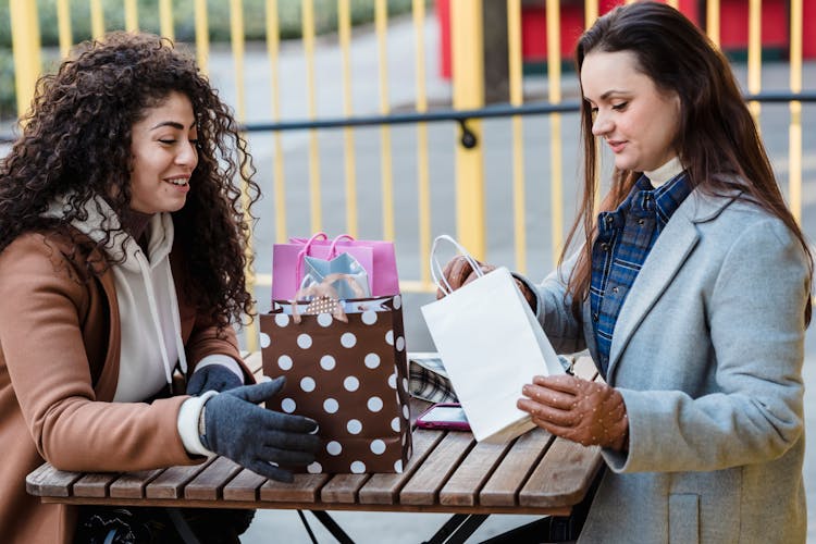 Women At Table Unwrapping Gift Packages In City Street