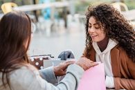 Women checking gift packages at table in street