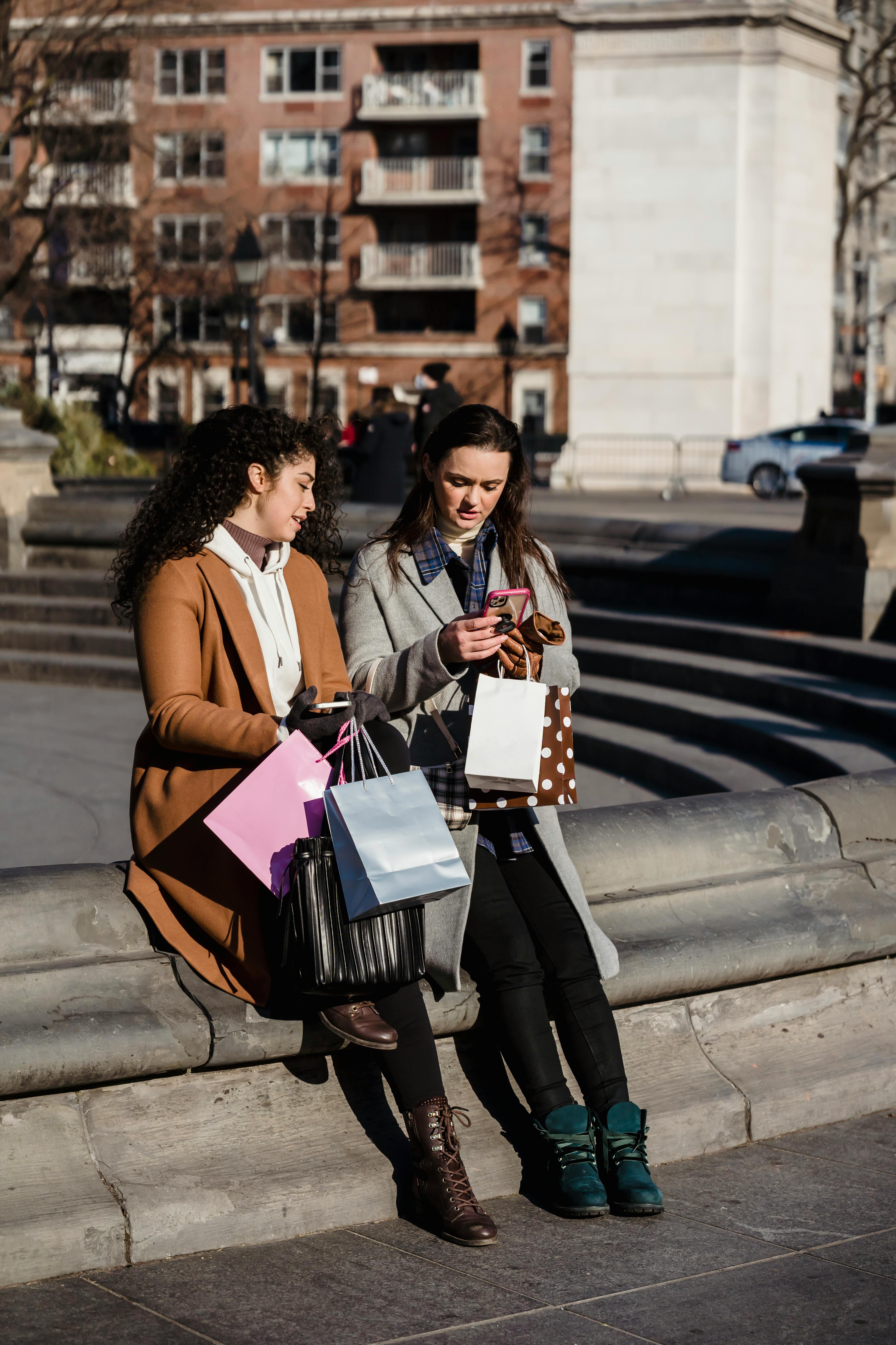 content women with shopping bags and smartphone sitting on street