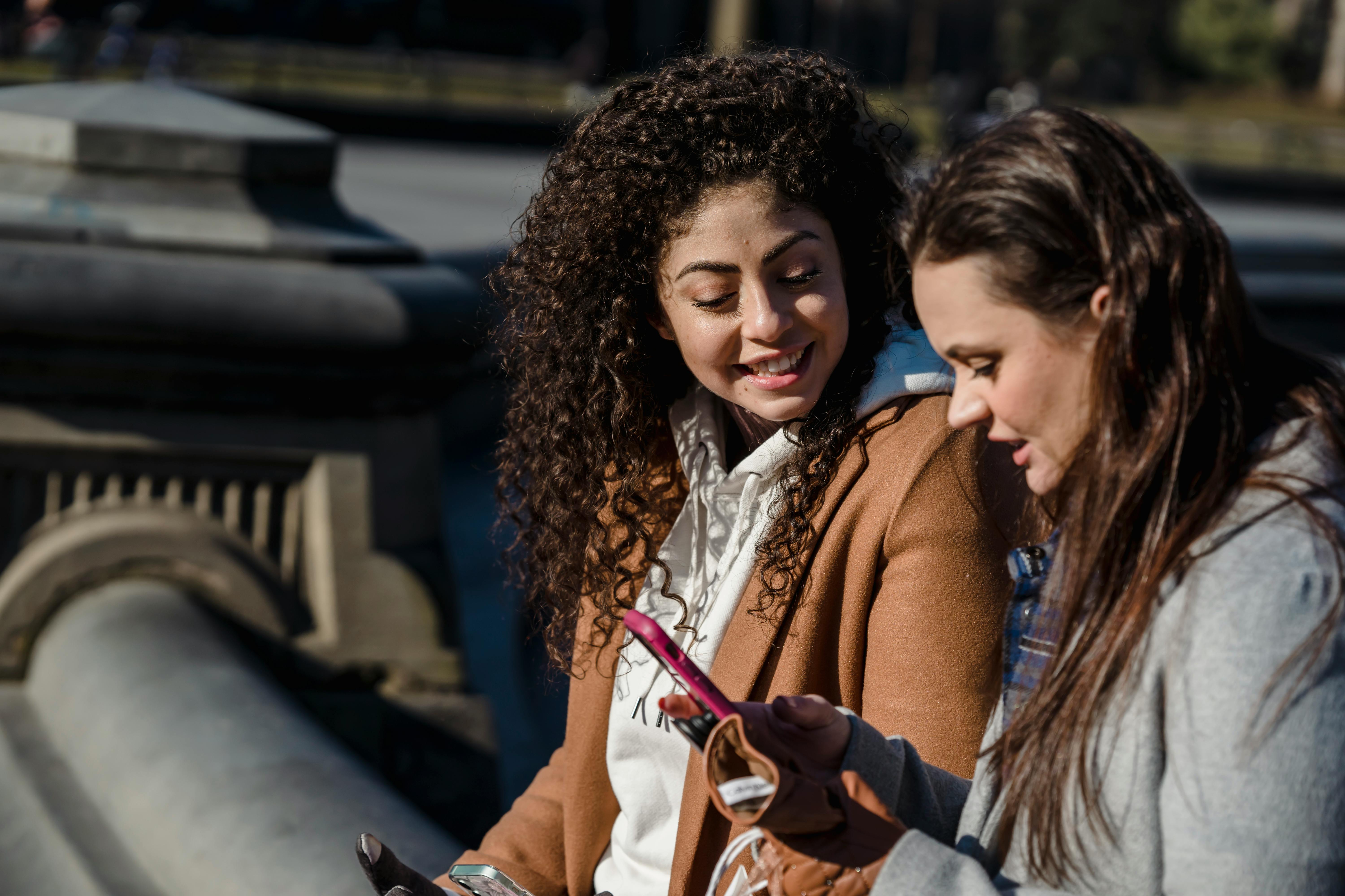 happy women using smartphone on city street on spring