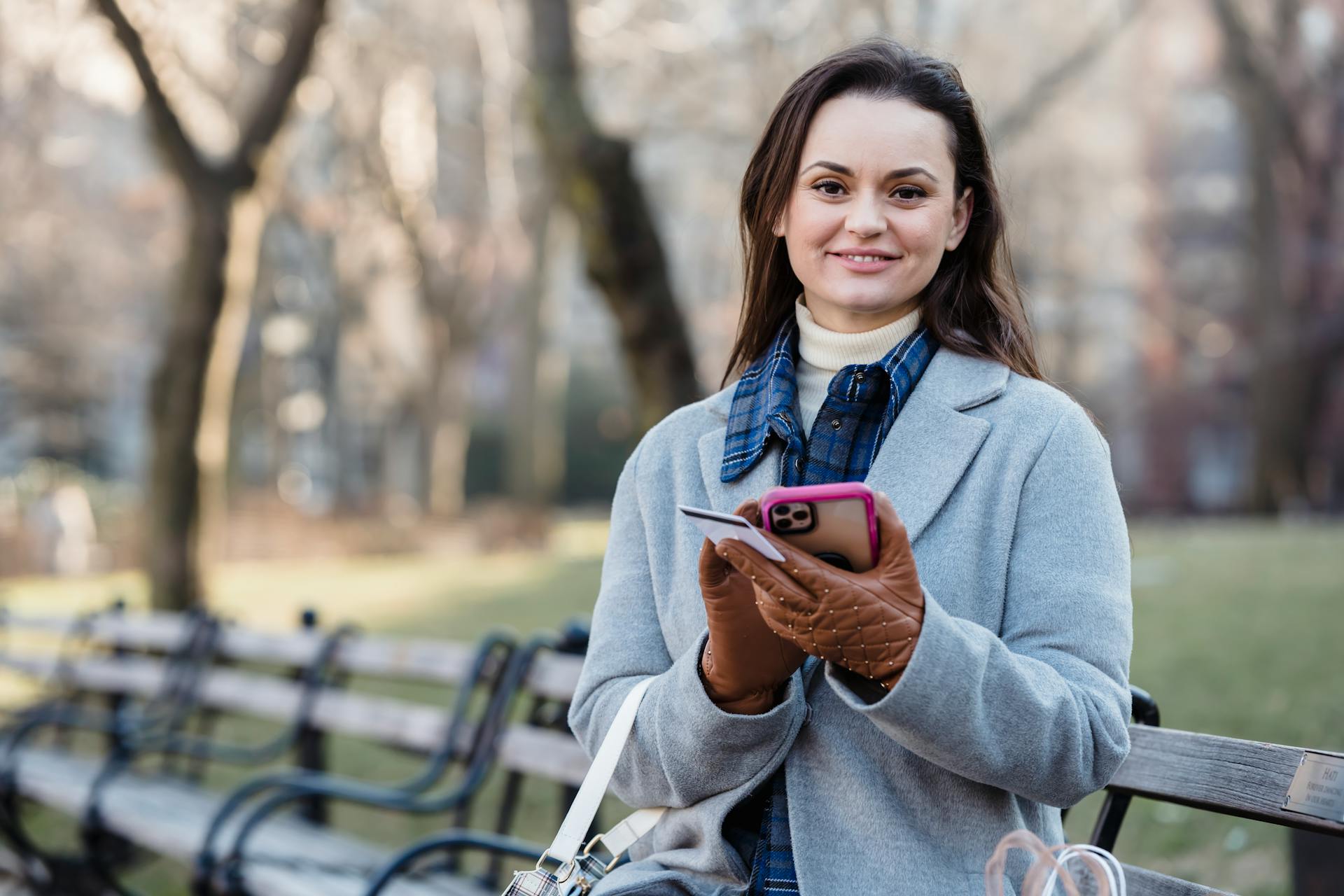 Cheerful young woman using smartphone and credit card in a sunny park.