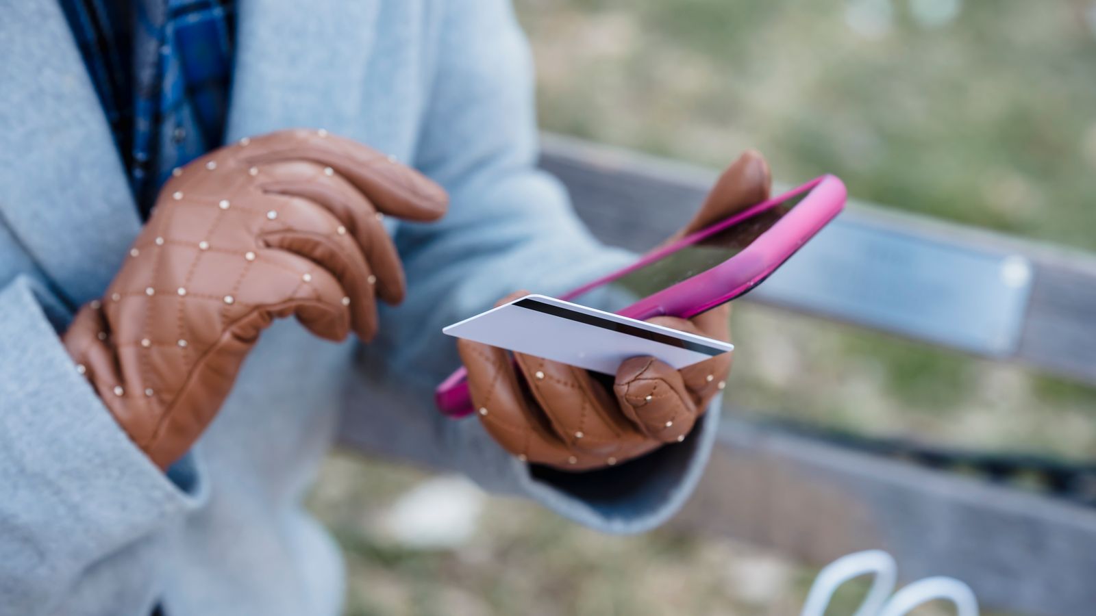A woman looking at her phone while holding a credit card near a laptop