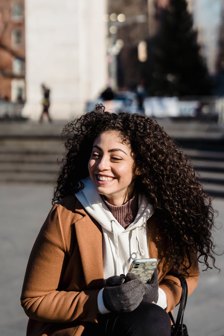 Joyful Woman With Smartphone Sitting On Sunny Spring Street