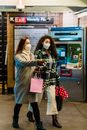 Women friends in protective masks and casual clothes with shopping bags walking in subway hallway during coronavirus