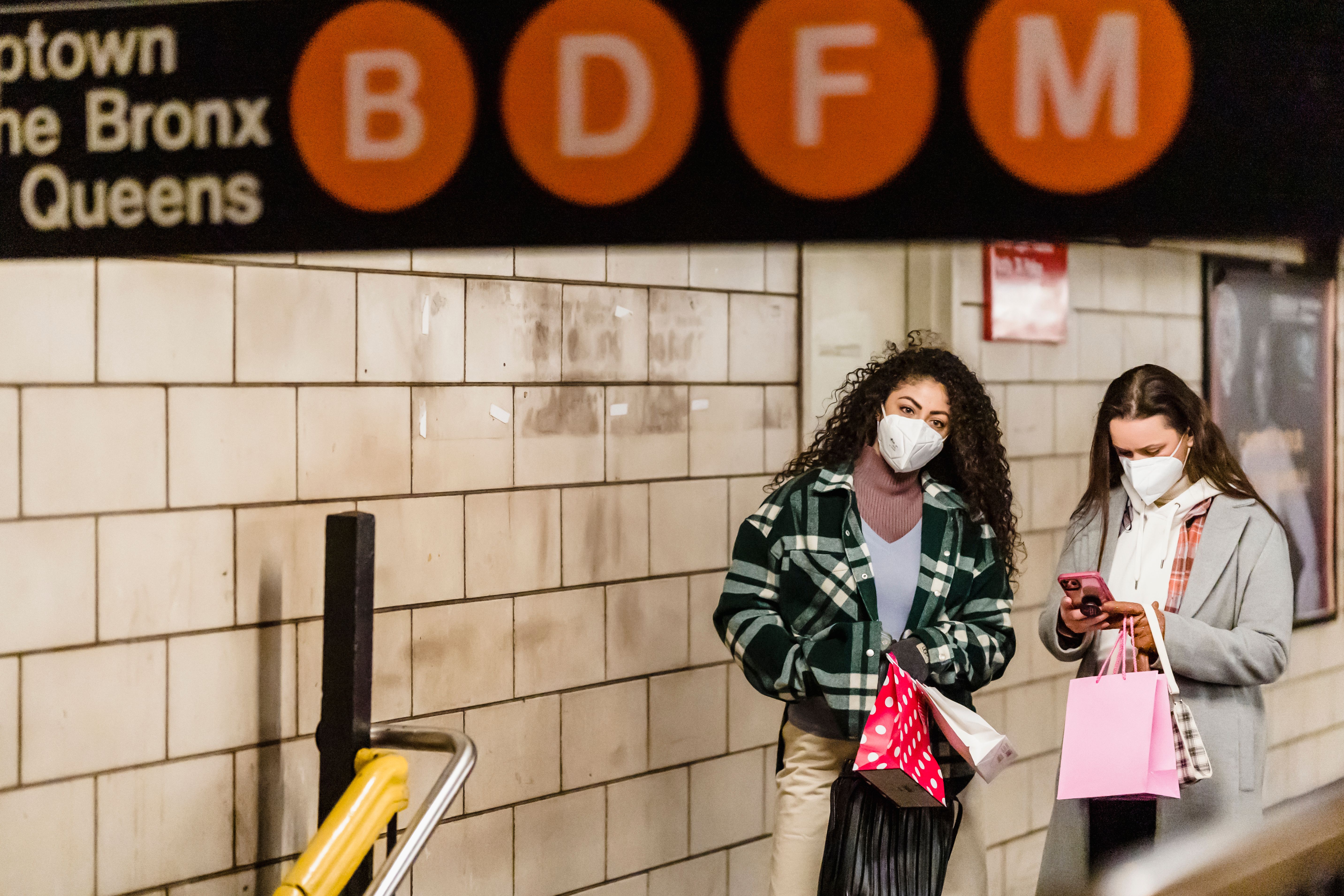 Calm women friends in protective masks standing with festive shopping bags standing in subway passage during coronavirus