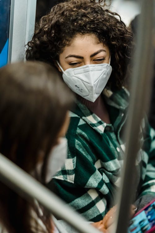 Female with curly hair in sterile mask sitting in train