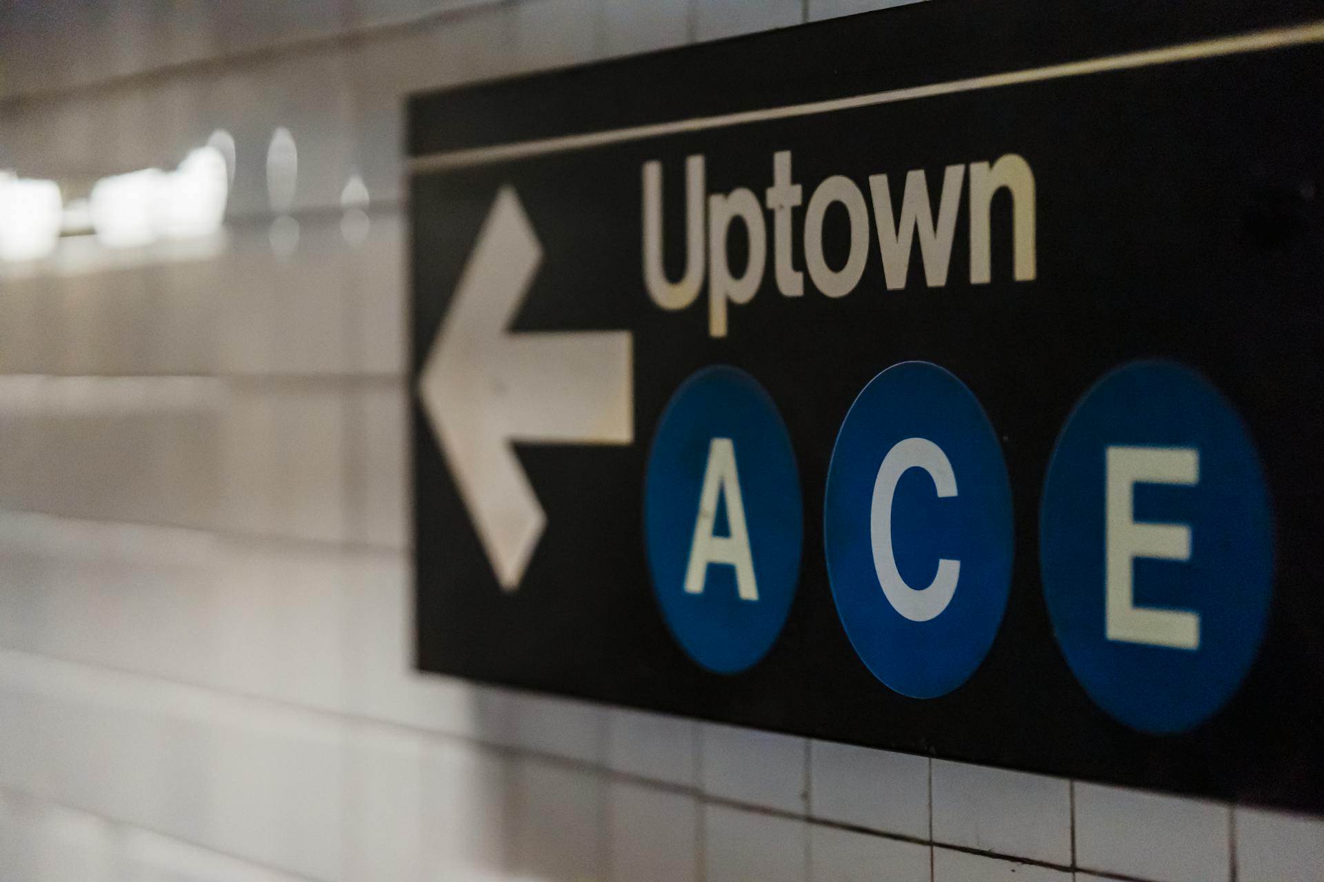 Close-up of an Uptown subway sign with directional arrow and A, C, E lines.