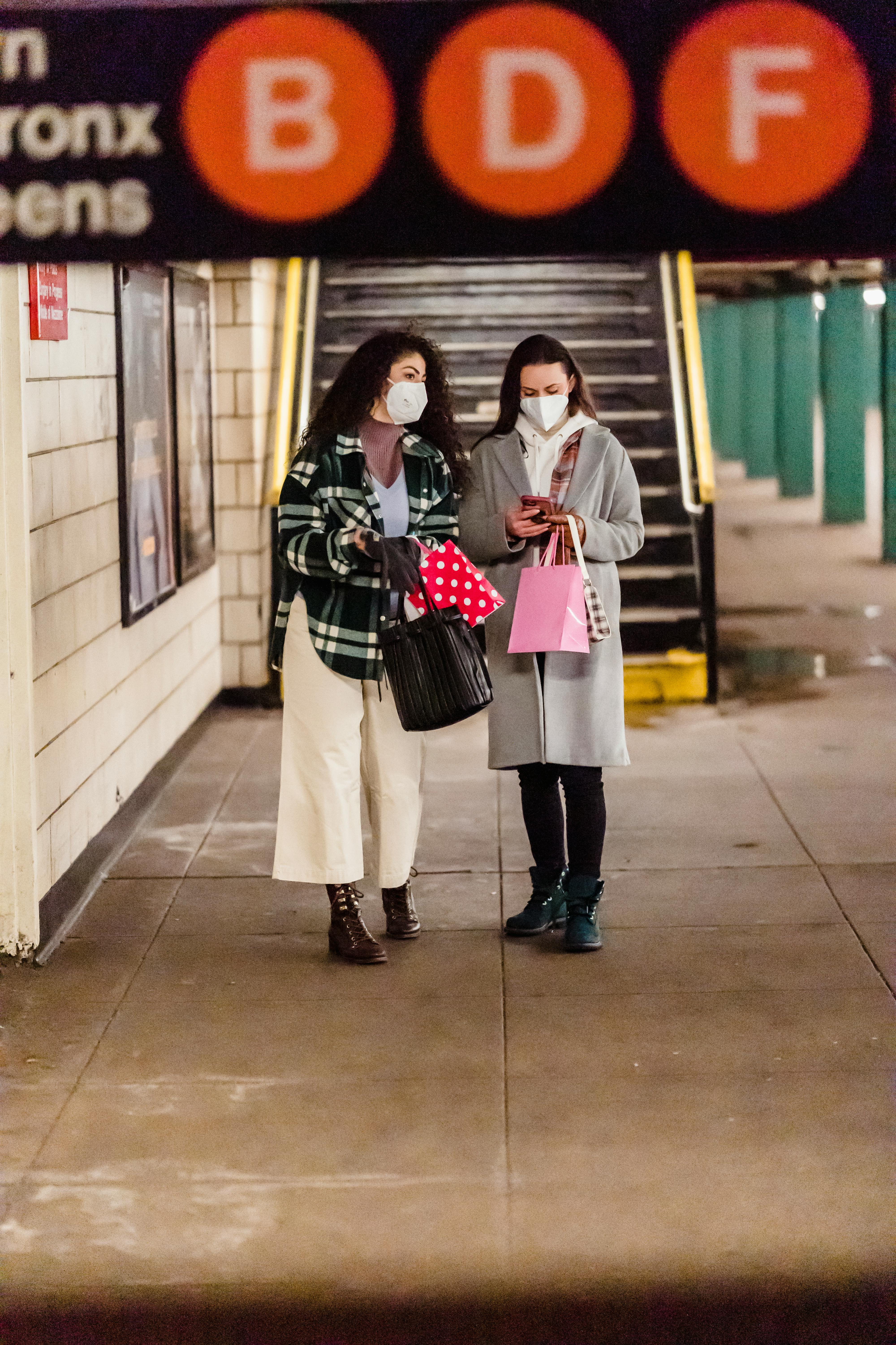 girlfriends in masks with bags using cellphone in underground station