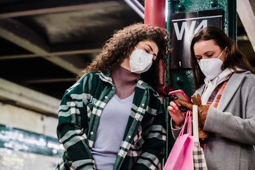 Free Girlfriends in masks using cellphone with paper bag in metro Stock Photo