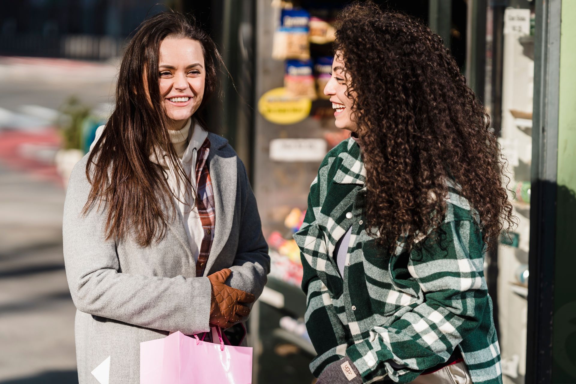 Smiling young women in warm clothes and gloves with shopping bags standing on city street on pavement in sunny day