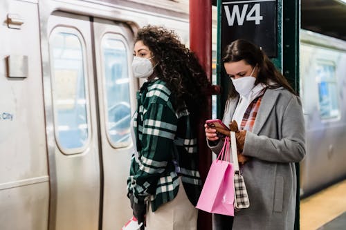 Girlfriends in masks using cellphone in underground station near train