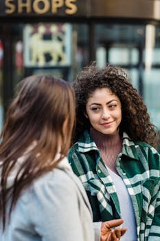 Two young women chatting in a lively city street, capturing a moment of friendship.