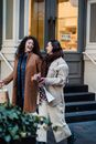 Young positive female friends with shopping bags speaking and laughing happily and looking at each other while strolling after visiting shop