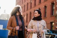 Low angle of positive female friends talking to each other while carrying paper packets after shopping together