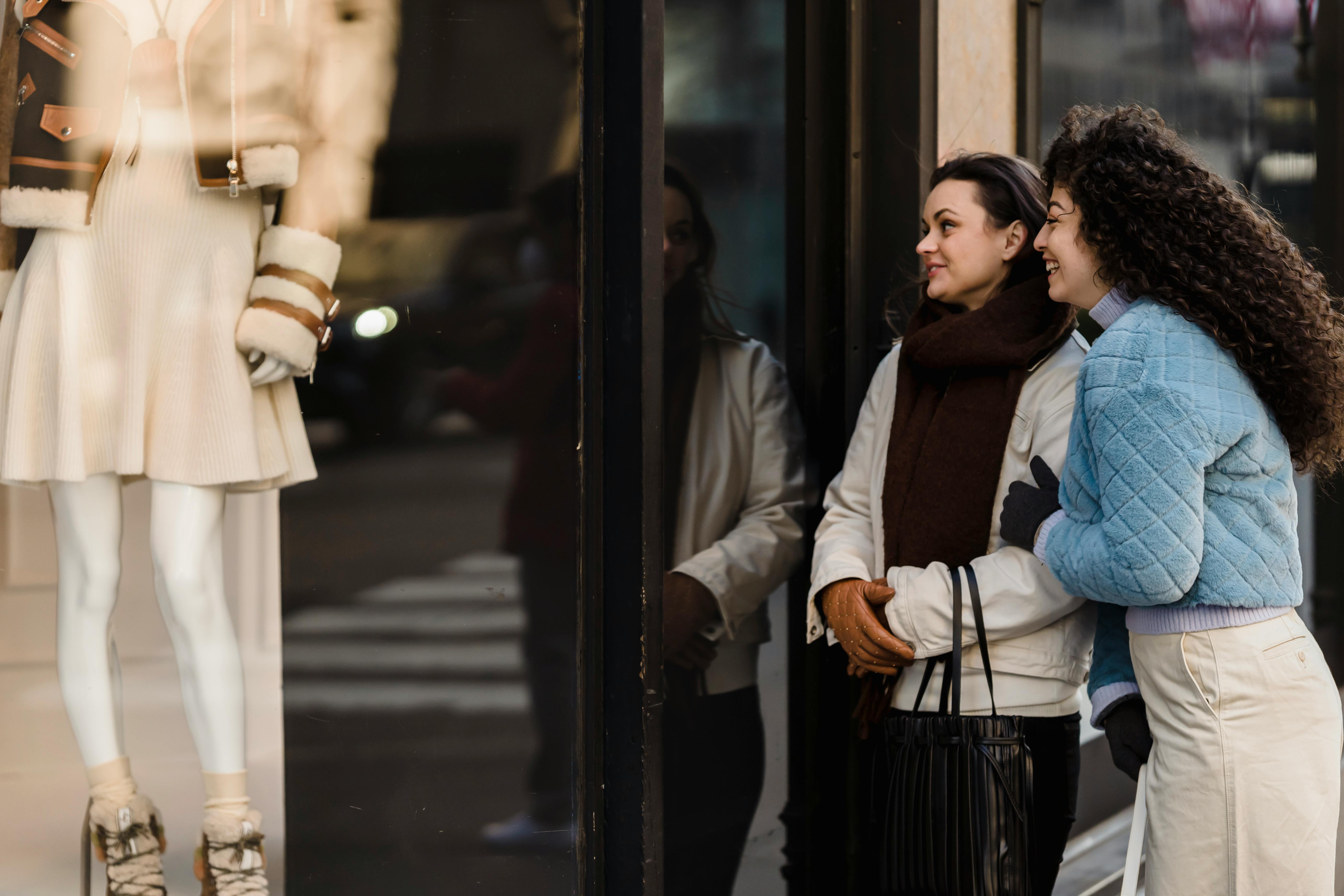 positive young female friends looking through showcase of boutique