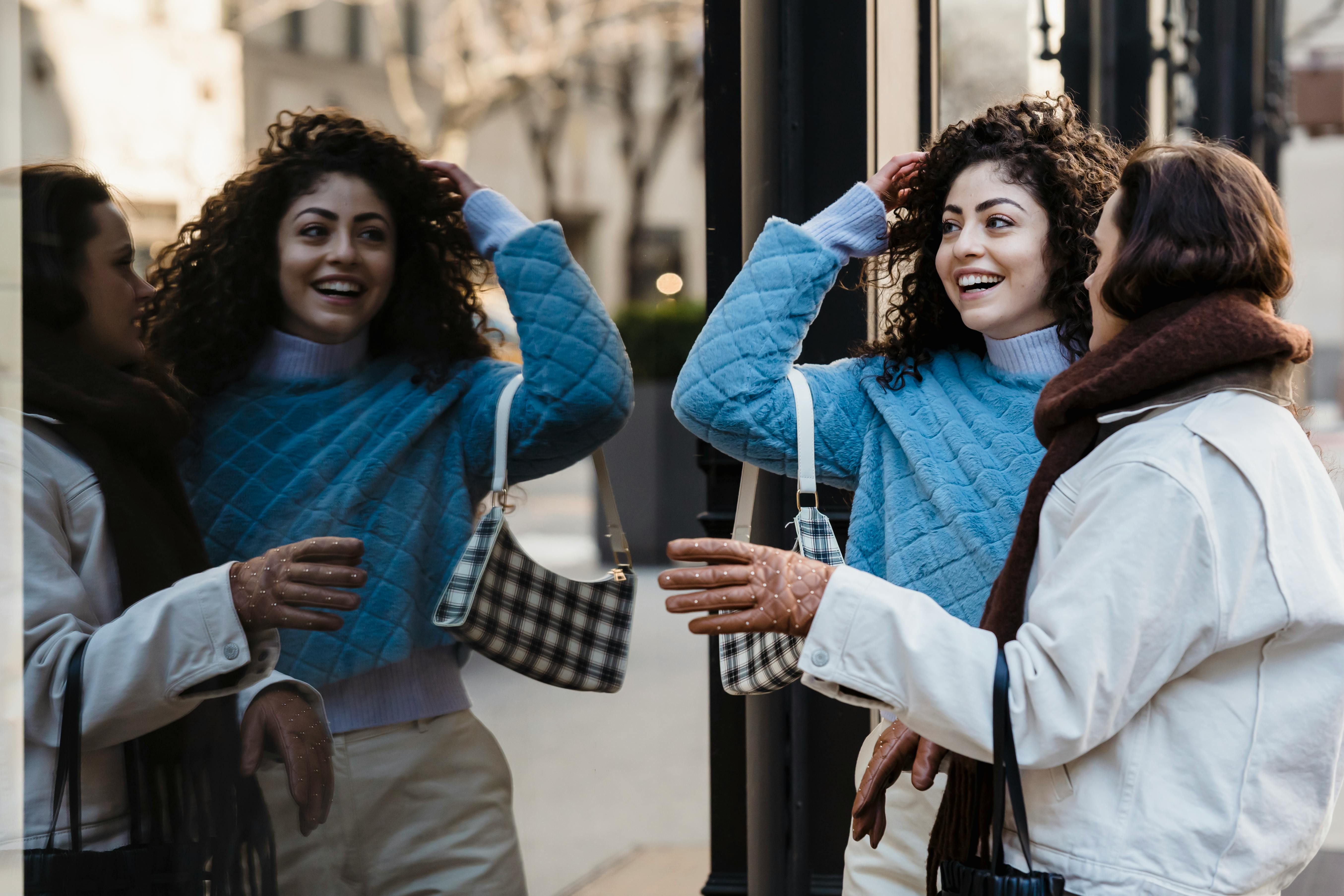 positive female friends standing together near reflecting wall