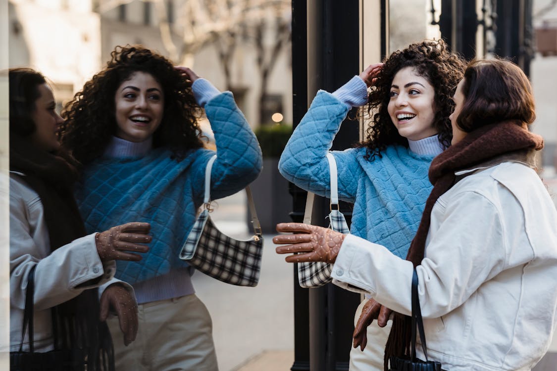 Positive female friends standing together near reflecting wall