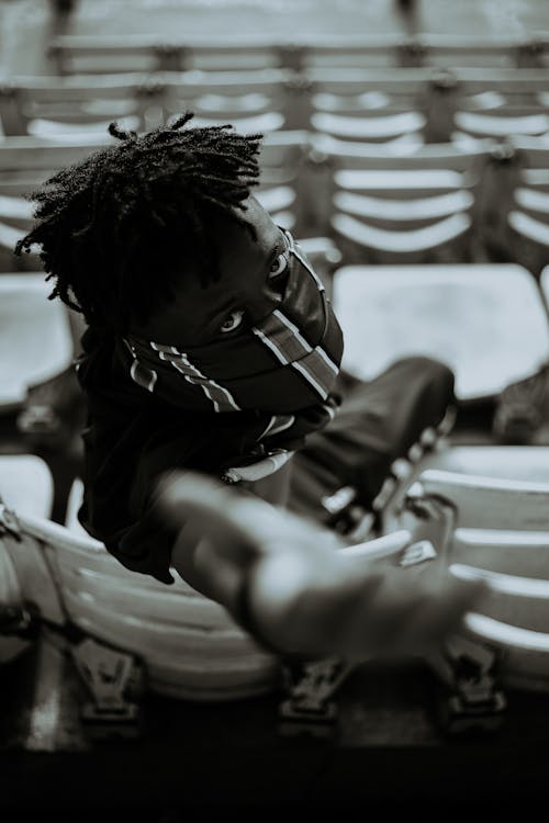 Black man sitting on tribune and reaching out hand towards camera