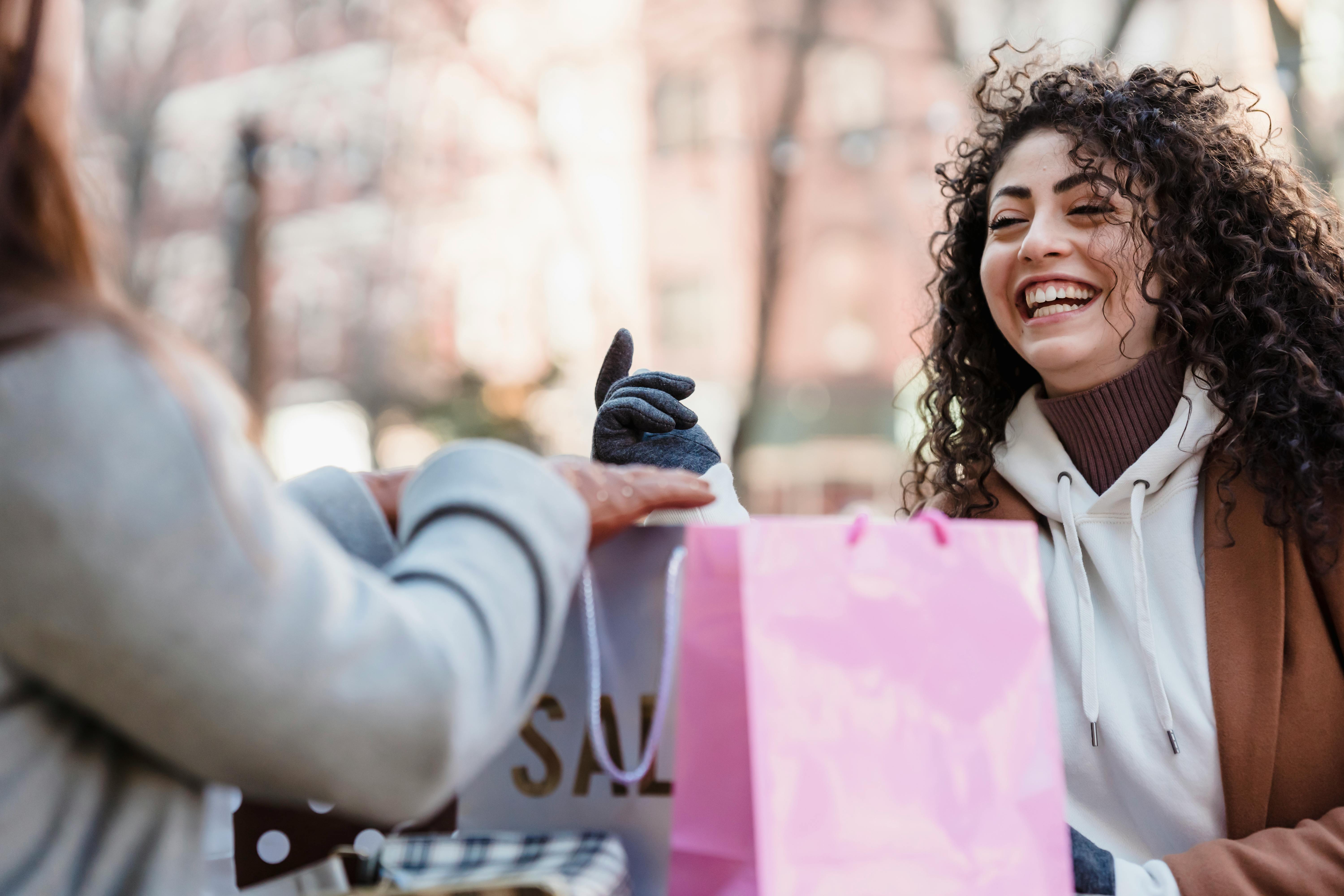 Two women enjoy a cheerful conversation while shopping outdoors, sharing joyful moments.