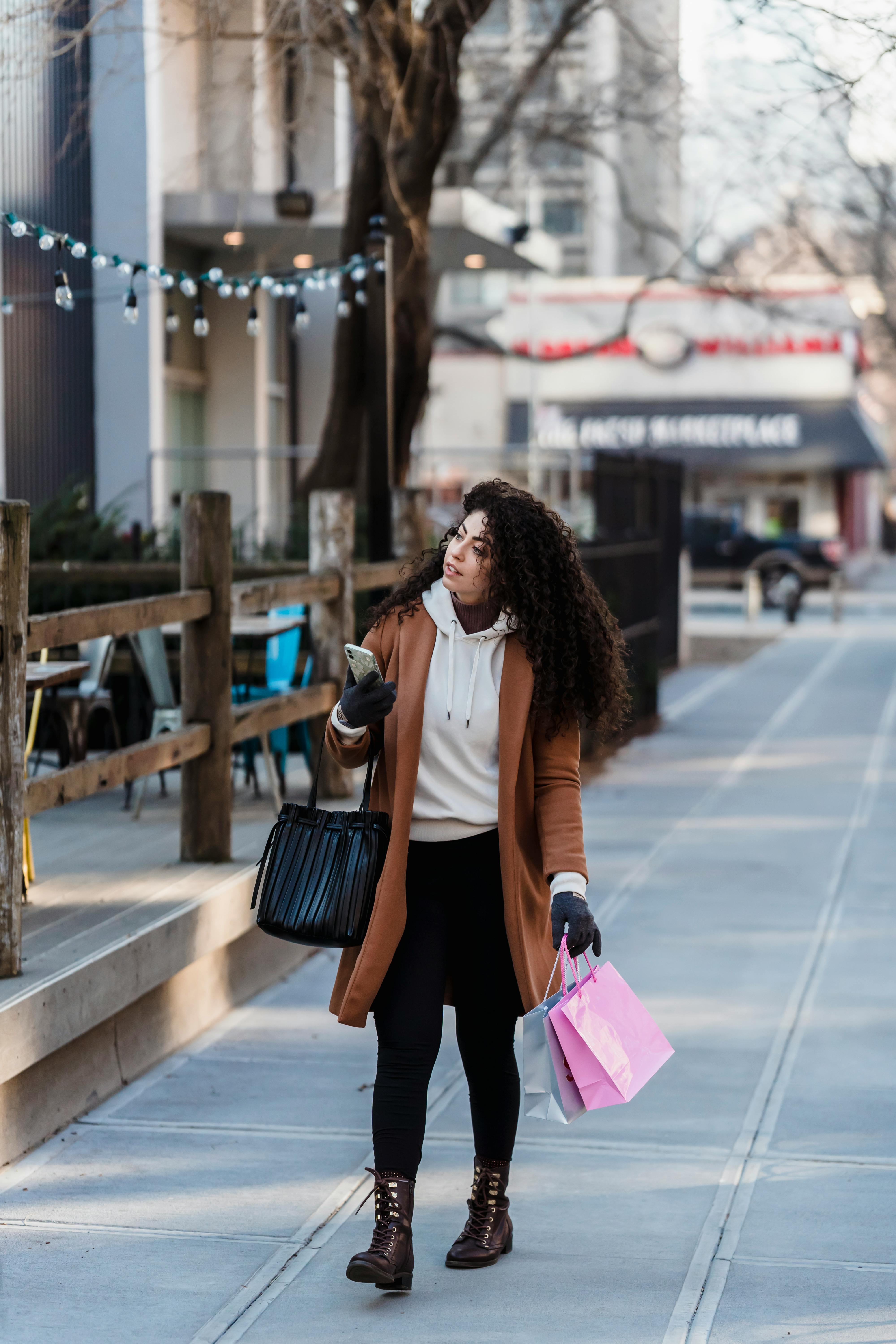 attentive female carrying shopping bags while walking with smartphone