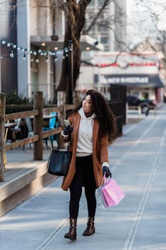 Young woman walking in city with shopping bags and smartphone, exploring urban retail.