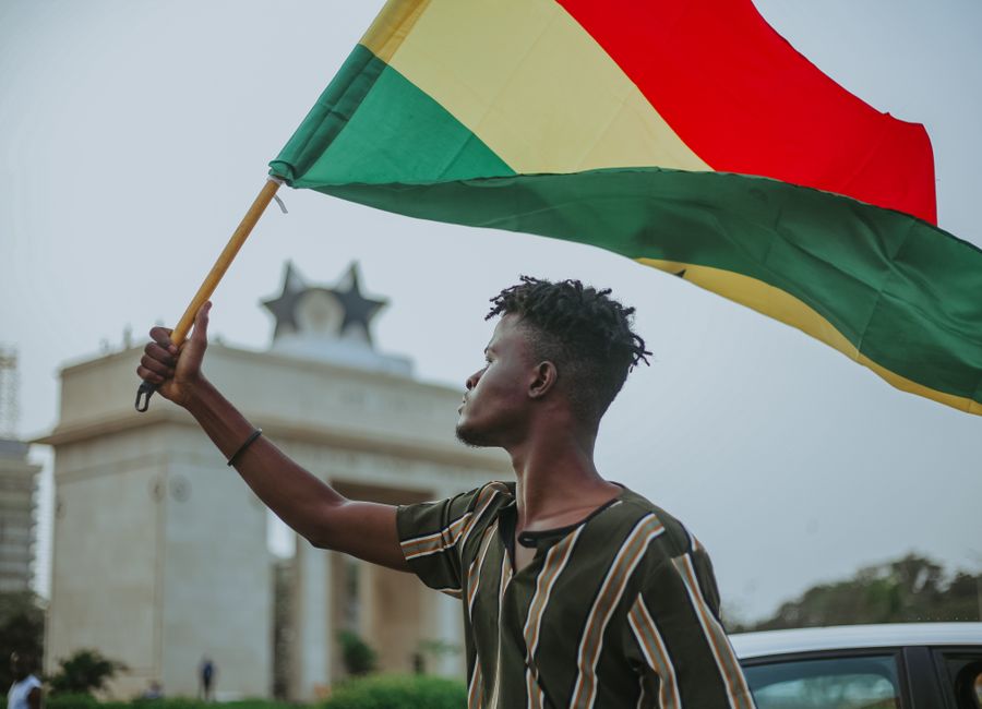 African male with dreadlocks raising flag of Ghana country with colorful stripes while looking away in town