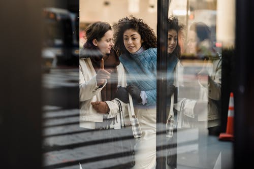 Free Through window of positive multiracial female friends standing near glass wall of modern shop while standing on street in city Stock Photo