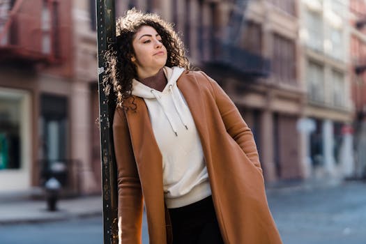 Fashionable woman in coat leans against a pole in a city street.
