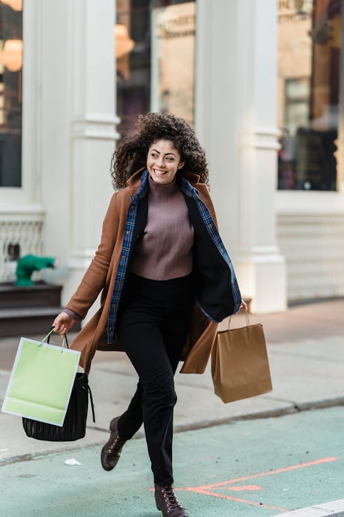 Free Cheerful ethnic woman with shopper bags running on road Stock Photo